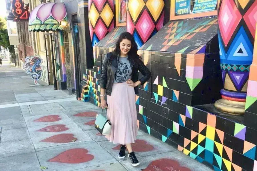 A woman stands on a sidewalk painted with red hearts, in front of a colorful storefront, in San Francisco's Haight-Ashbury neighborhood.